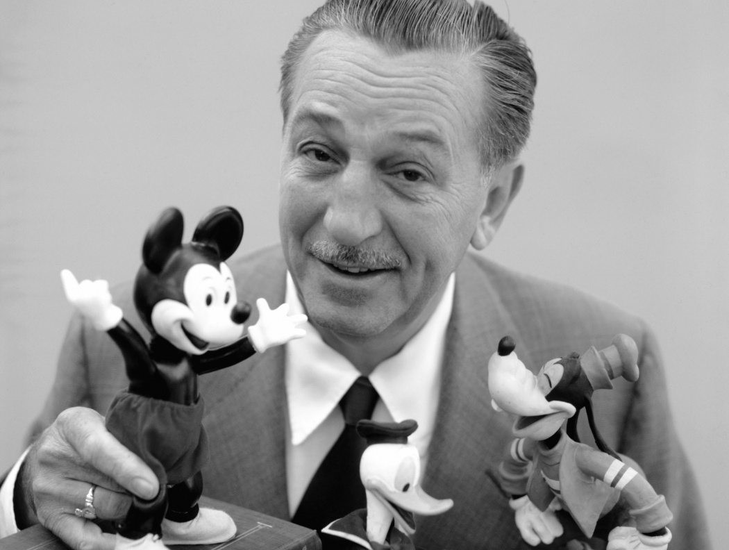 Walt Disney sitter med leksaksfigurer av Musse Pigg, Kalle Anka och Långben.