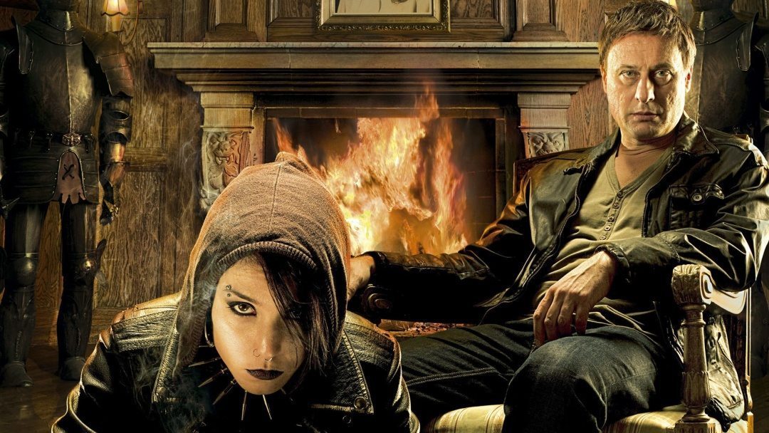 Noomi Rapace och Michael Nyqvist i Män som hatar kvinnor. De sitter framför en öppen spis och tittar in i kameran.