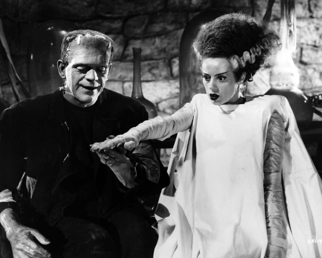 Ur Frankensteins brud. Monstret till vänster håller handen med den kvinnliga skapelsen som stirrar tomögt ut framåt.