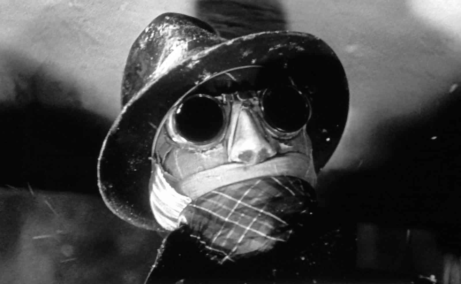 En närbild på Den osynlige mannen. Han har på sig sina svarta solglasögon och hatt. Hans ansikte är inlindat i bandage.