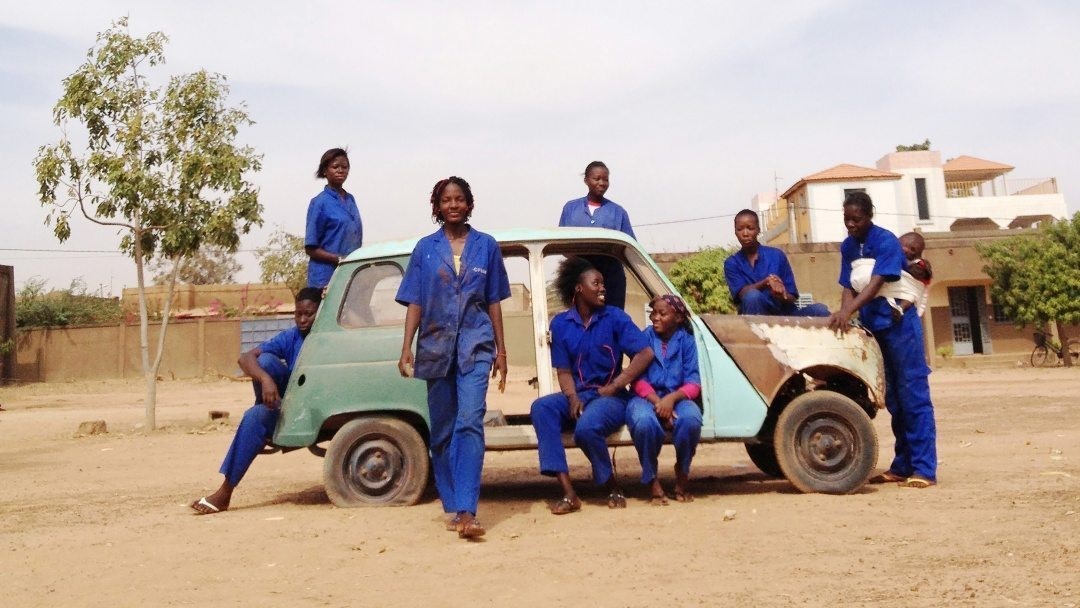 Från Ouaga Girls, en dokumentärfilm av Theresa Traore Dahlberg. Kvinnorna står i blåa arbetskläder utomhus runt en turkos bil.