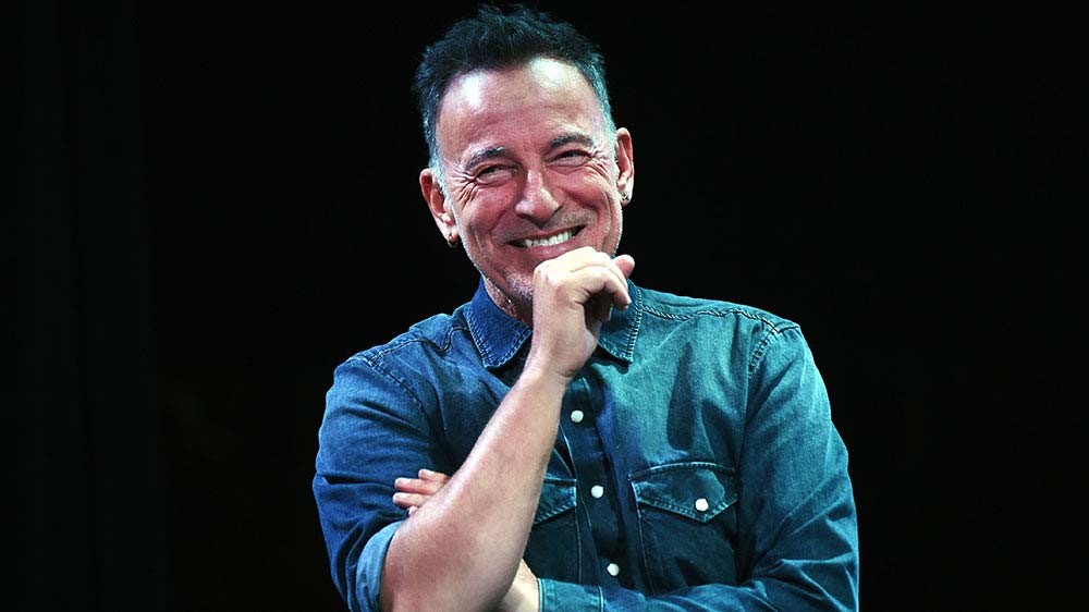 Bruce Springsteen håller i en mikrofon och ler.