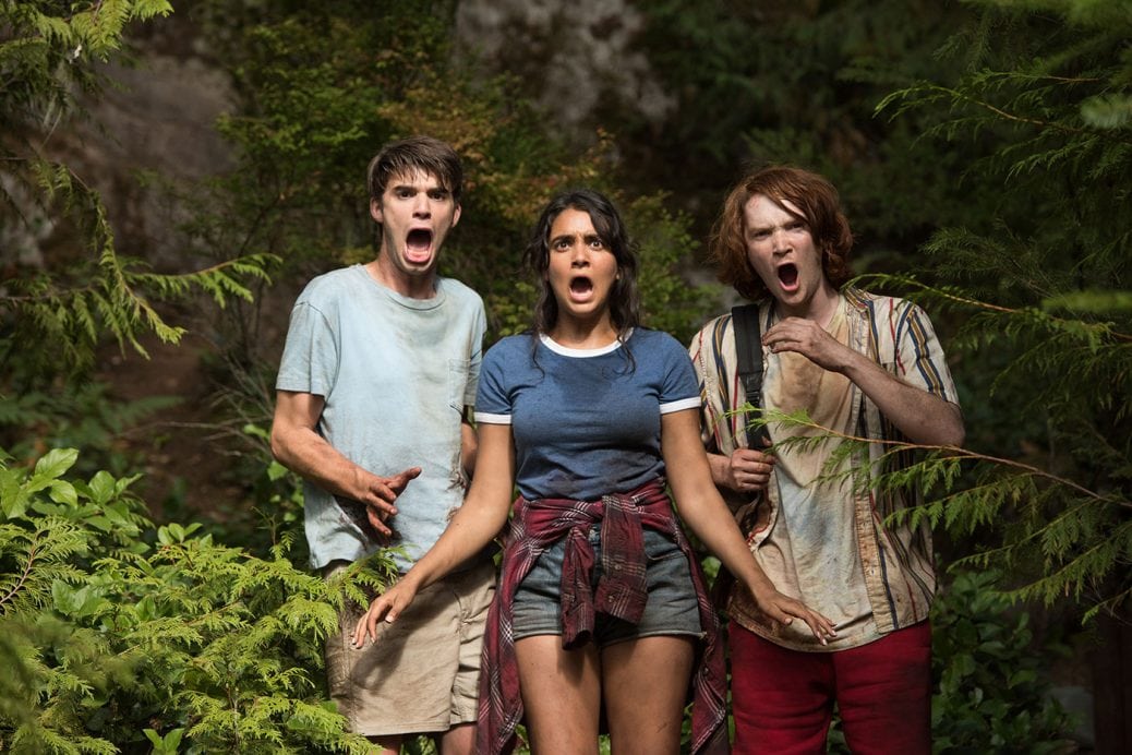 Tre av ungdomarna står i skogen och stirrar förfärat med öppna munnar. 