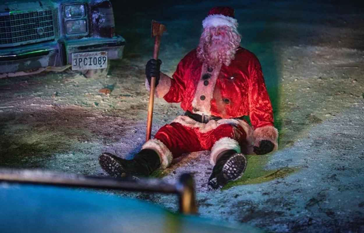 Den mordiska tomten sitter på marken med en yxa.